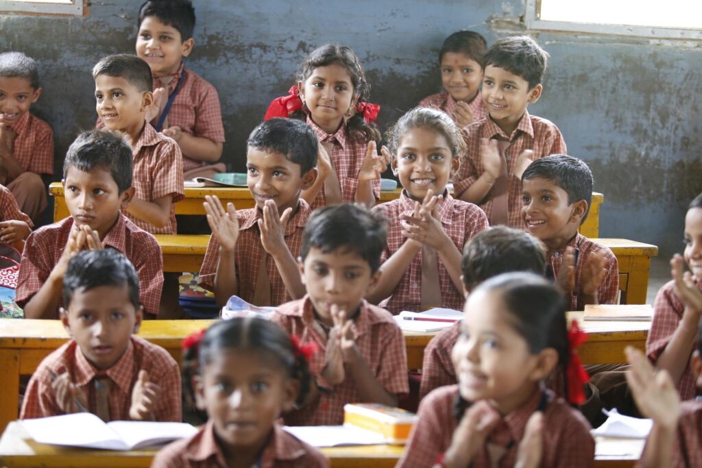 A classroom of smiling primary school children in uniform clapping and learning together.
