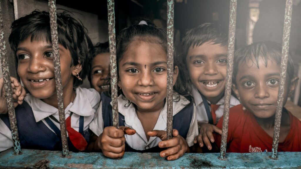 Smiling school children looking through a classroom window grille, symbolizing hope and the barriers they overcome to access education.