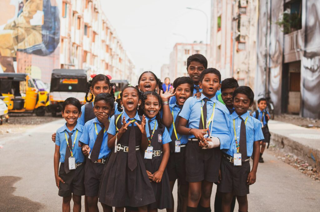 Smiling school children in India looking through window bars, representing hope and the need for educational support.