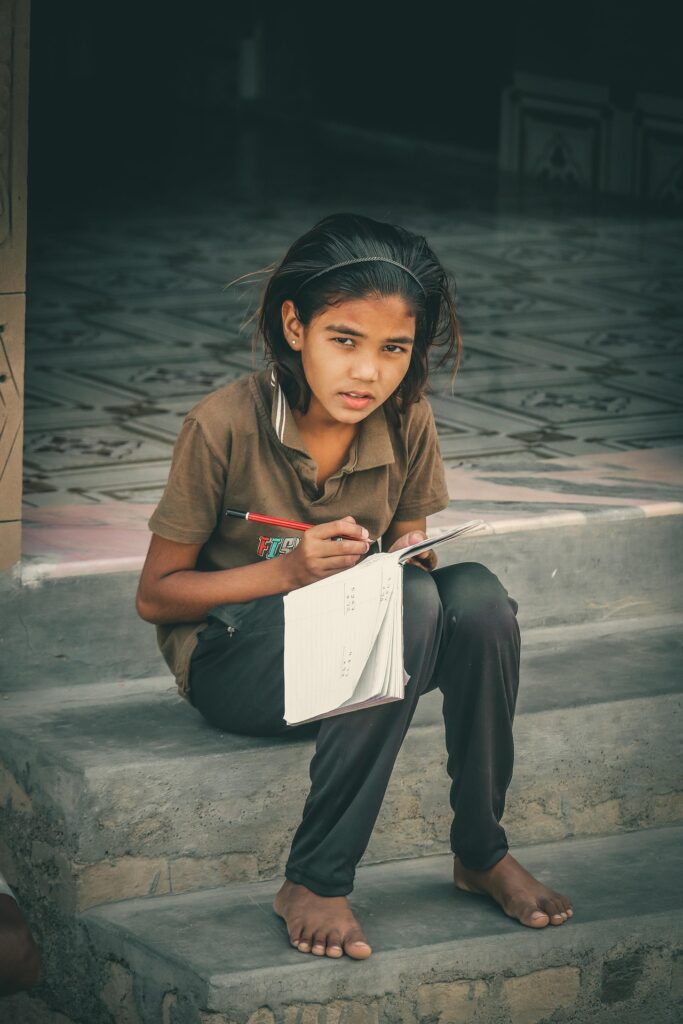 Young Indian girl sitting on steps and writing in a notebook